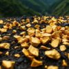 Gleaming gold nuggets on a dark surface with mountains.